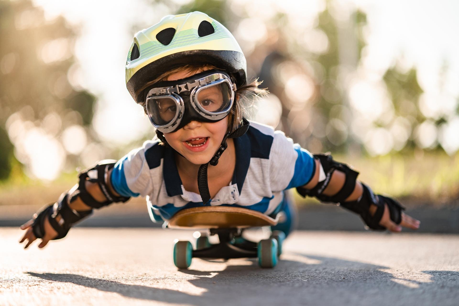 Foto van jongen met helm en vliegbril die met zijn armen wijd op een skateboard ligt
